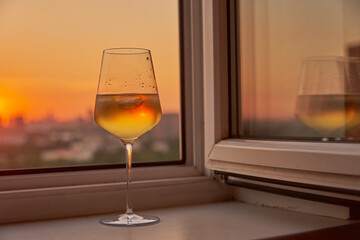 A glass of wine on the windowsill against the background of the sunset.