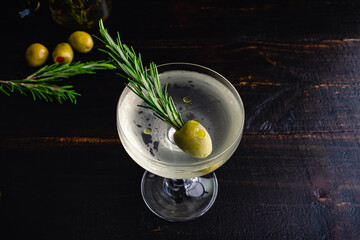 Smoked Rosemary Oil Dirty Martini: A dirty gin martini served up in a coupe glass and garnished with a sprig of rosemary in a green olive - obrazy, fototapety, plakaty