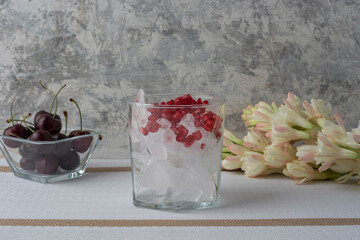Vaso de cristal con hielos y granada acompañado de cerezas y una flor