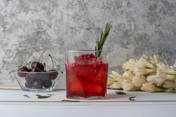 Bebida de arándano con hielos, granada y una rama de romero, acompañado de cerezas y flores