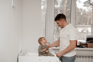 Male babysitter prepares the child for sleep in the middle of the day, smiles and explains to the child that it's time to sleep