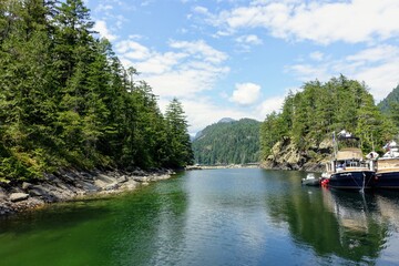 Two boats anchored anchored side by side in a beautiful scenic bay surrounded by forests and mountains, in British Columbia, Canada.