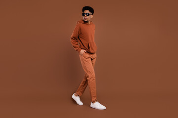 Full body profile photo of nice short hairdo young guy look empty space dress spectacles sportswear trousers sneakers isolated on brown background