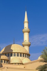 Minaret and dome of a Muslim islamic mosque on the background of the blue sky. Minaret tower and roof cupola with traditional crescent, architectural decorative elements.