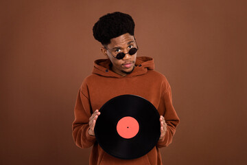Photo of confident dj african guy hold vinyl disc look camera wear sunglass sweatshirt isolated on...