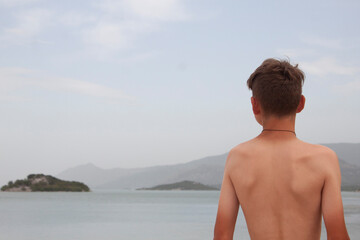 the boy stands in the water and looks at the sea