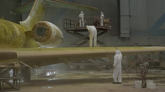 Preparing the aircraft for painting.
General plan of the hangar with the aircraft. Workers in white protective suits and respirators prepare the plane for painting.