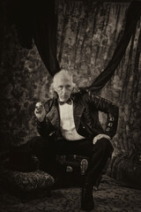 Stylized, antiqued portrait of victorian steampunk, sitting with hand on knee and holding pipe,...