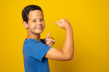 Strong boy showing muscles, isolated on yellow background