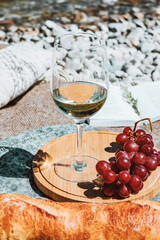 Summer romantic rustic picnic on the coast with white wine glass, baguette, cherries, grape, open book, pillow. Sea beach. Vacation, rest in Europe. Alcohol drink close up.