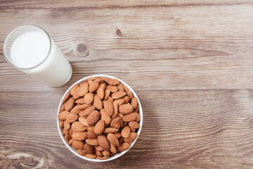 Almond nuts in a white bowl and milk in glass on wooden background, top view, flat lay, top-down, selective focus.copy space.