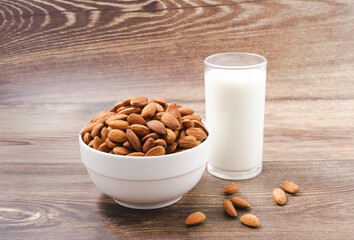 Almond nuts in a white bowl and milk in glass on wood background with nuts around the bowl.selective focus.front view.