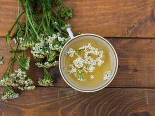 medicinal plant yarrow, a mug with a decoction of yarrow flowers on a wooden background