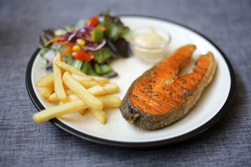 Grilled Salmon steak with salad and friend fried selective focus blur gray background with copy space.