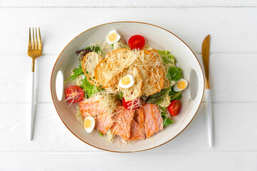 Caesar salad with grilled chicken on white wooden background