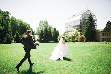 Stylish couple of happy newlyweds. Bride running from groom in the park on their wedding day with...