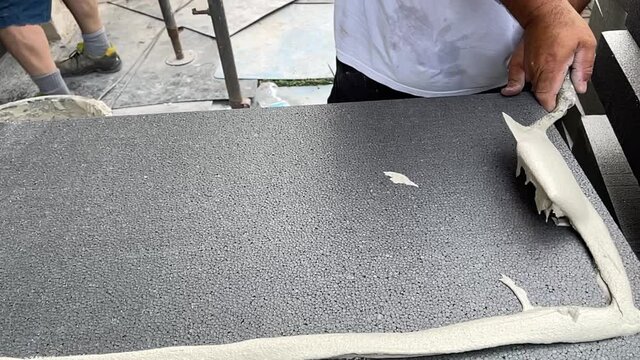 Man Spreading Building Glue on Thermal Insulation Panels before Their Application on the Facade of a House in Slowmotion