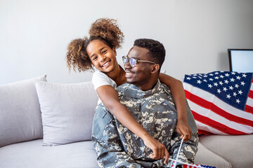 Photo of American soldier playing with his daughter at home. American soldier finally at home with his family. Family welcomes home USA army soldier. Home in background.