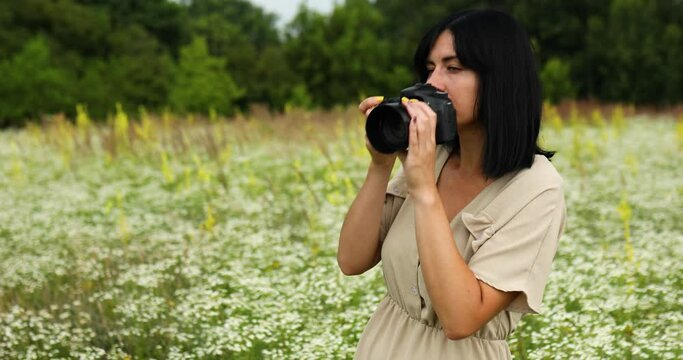 Female photographer take photo outdoors on flower field landscape holding a camera, woman hold digital camera in her hands. Travel nature photography