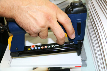 selective focus, man stapling notebooks with air stapler at printing press	
