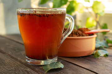 A cup of chaga tea on a dark table. Chaga slices and birch twig