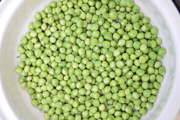 RAW baby peas in small white bowl, on table. Close-up
