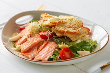 Caesar salad with grilled chicken on white wooden background