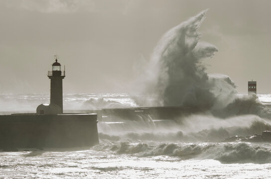 olas impactando en el rompeolas junto a un faro con el cielo nublado 