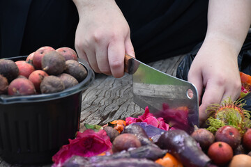 Homeowner is slicing rotten fruits and vegetables on wooden table in the backyard to mix together...