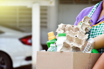 Homeowner is carrying black plastic bag which fulled with garbages, plastic bottles, cartons, milk bottles and used paper to separate and manage garbages at home. Soft and selective focus on garbage.