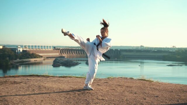 Translation: Kyokushinkai. young woman white kimono demonstrates karate technique against backdrop nature