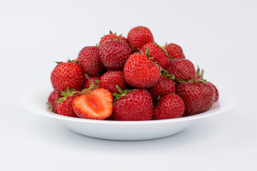 On a white background, a white plate with ripe strawberries.