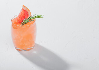 Red grapefruit cocktail with fruit slice and rosemary on white background.