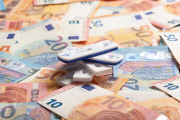 Rapid diagnostic tests lying on top of pile of money symbolizing making business thanks to COVID-19 pandemic