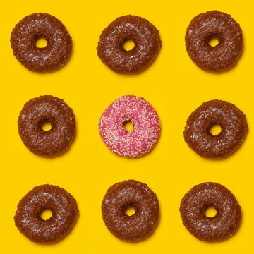 Pattern of brown doughnuts with single pink one in middle