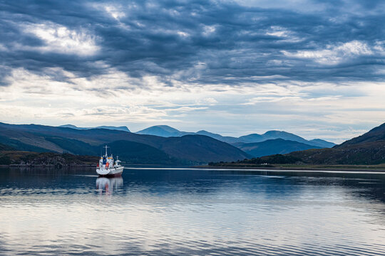 UK, Scotland, Ullapool, Clouds over lone fishing boat sailing across bay in Scottish Highlands