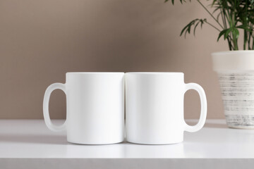 Two mugs mockup with workspace accessories, green plant in pot on beige table. Front view. Place for text, copy space, mockup
