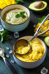 Diets vegetarian summer Ice cream or sorbet, sweet snack or dessert. Homemade avocado and mango fruit ice cream, tropical fruit sorbet on a dark stone table.