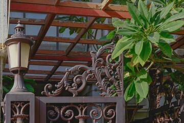 Fragment of vintage handicraft ornate forged front group with wrought elegant lattice gate and lantern and growing tropical tree Decorative design of the entrance of forged metal.