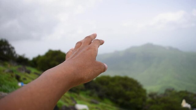Closeup shot of hand of an Indian female in front of the green Girnar mountain at Junagadh, Gujarat, India. Young girl extends her hand towards mountain. Girl seeking hope concept.