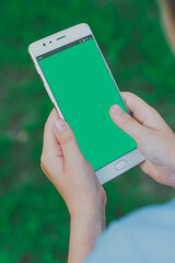 Concept of gaming, education. Smartphone with green screen in hand kid. Kid using phone during sunny day at park. The child is holding phone in his hand. Smartphone with hromakey, top view close up.