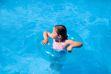 a child learning to swim is held for safety by a blue transparent inflatable circle in the sea, the...