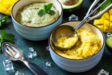 Diets vegetarian summer Ice cream or sorbet, sweet snack or dessert. Homemade avocado and mango fruit ice cream, tropical fruit sorbet on a dark stone table.