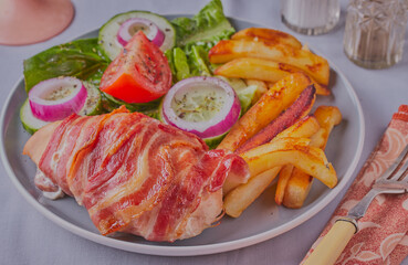 Chicken wrapped in bacon with salad and fries.
