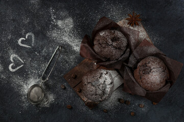 Chocolate coffee muffins with powdered sugar and cinnamon on a dark background. Two white hearts. Festive layout. Top view. Low key.