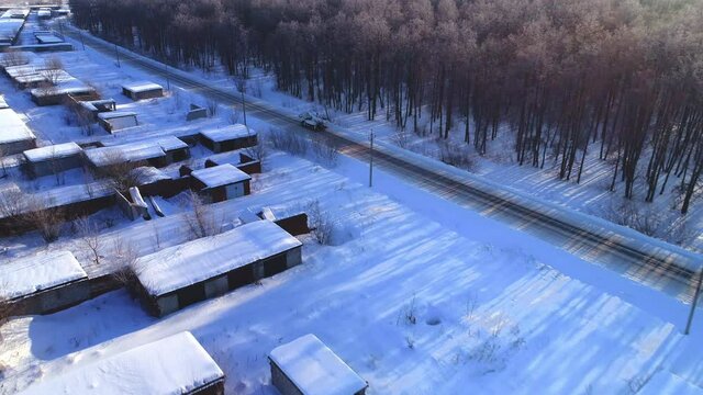 Hydraulic lifting truck drives along snowy rural road past bare tree forest and village in winter evening aerial view