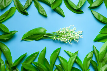Bouquet of lilly of the valley with green leafes as a floral frame. Flat lay with blue background. 