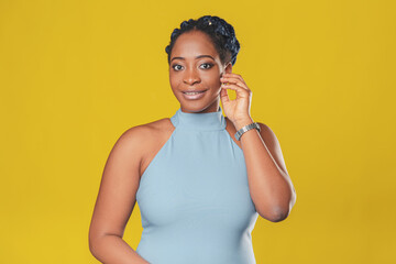 beautiful smiling african american girl in a blue dress, with pigtails hair rejoices on a yellow background