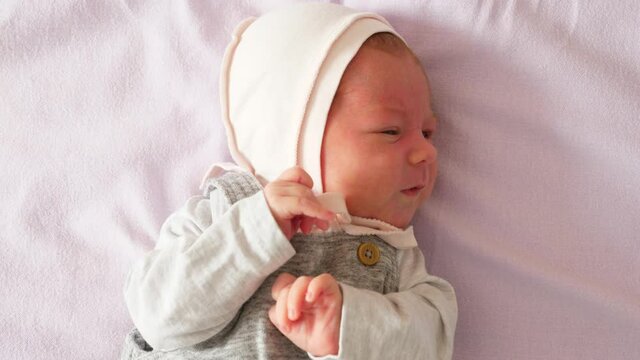 Infant baby cry loudly and yell for mother, portrait shot with original sounds. She shake tiny hands and turn head, lying alone at large bed