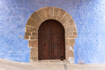 Fototapeta na wymiar Old and solid wooden door, in a church, with stone portico and blue facade. 